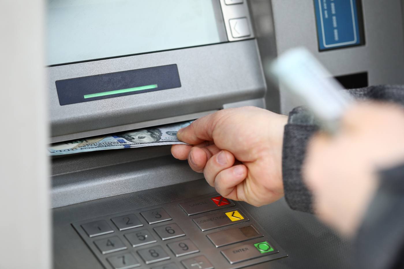 Person withdrawing cash from ATM machine with green light indicator