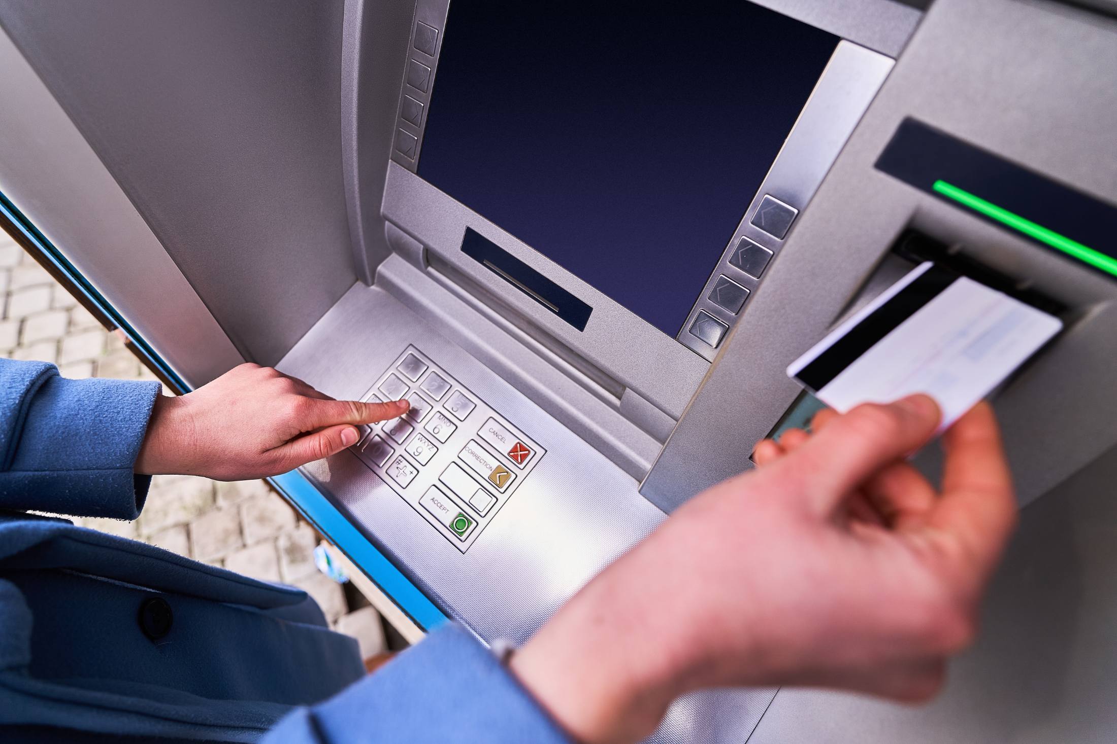 Person using ATM keypad to enter PIN while holding bank card