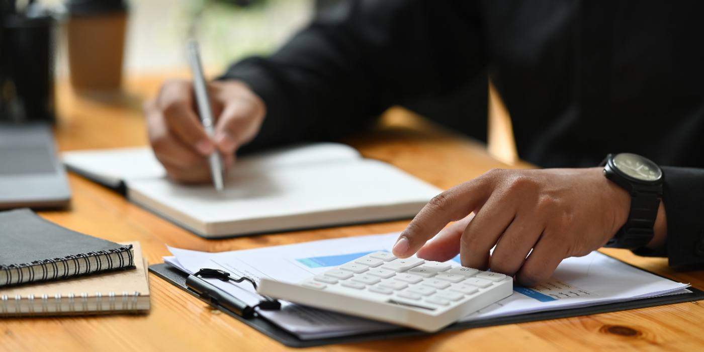 Professional using calculator at wooden desk with notepad and documents
