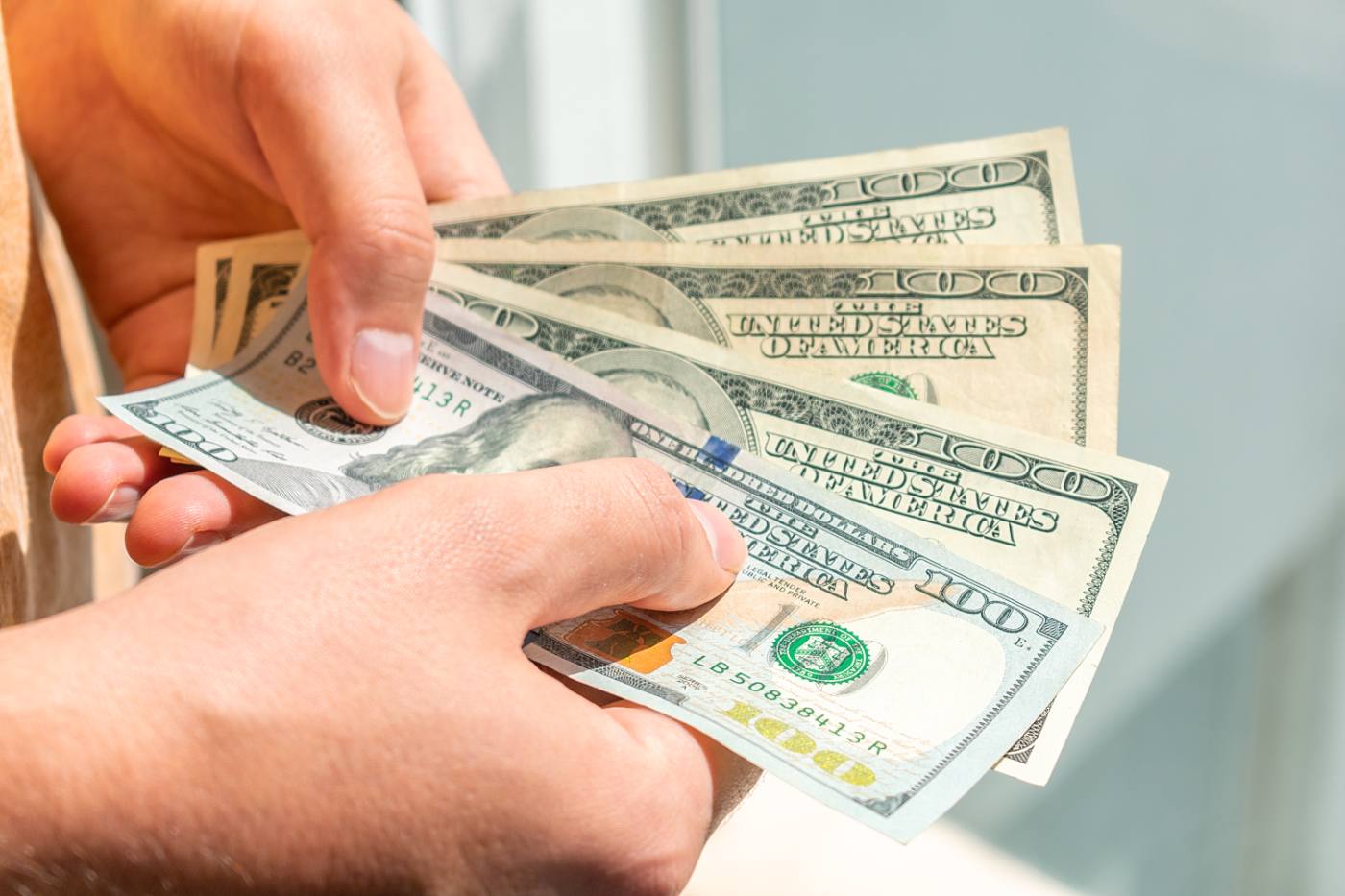 Person holding multiple one hundred dollar bills in their hands