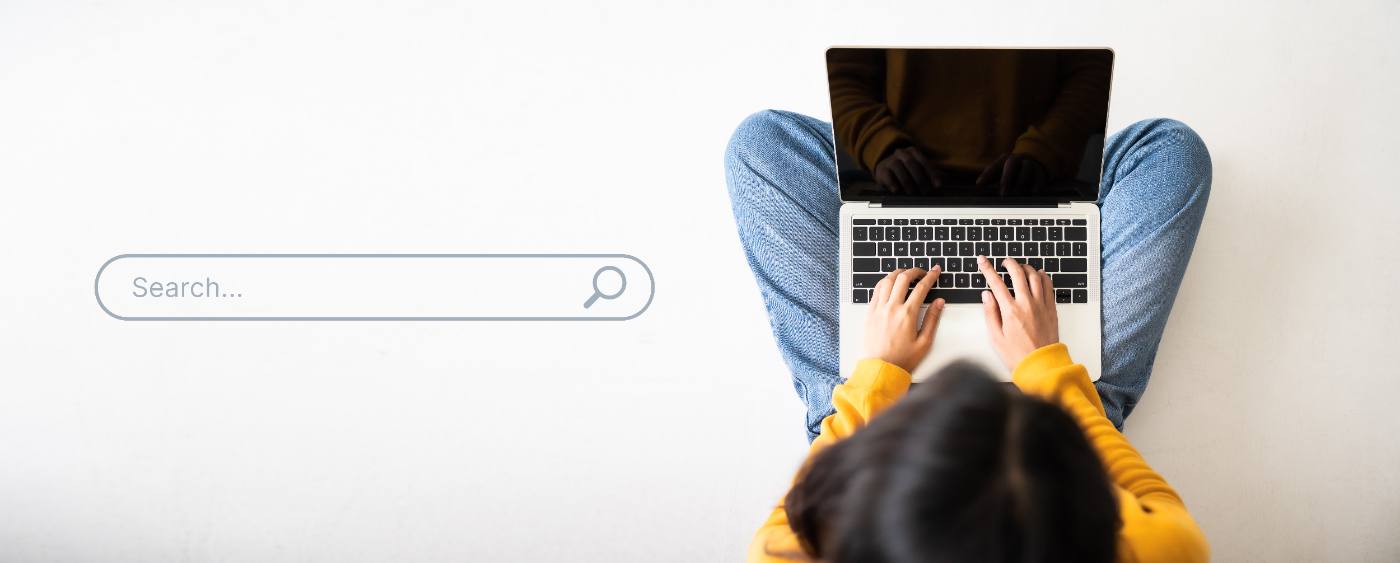 Person in yellow jacket typing on laptop while sitting cross-legged with search bar visible